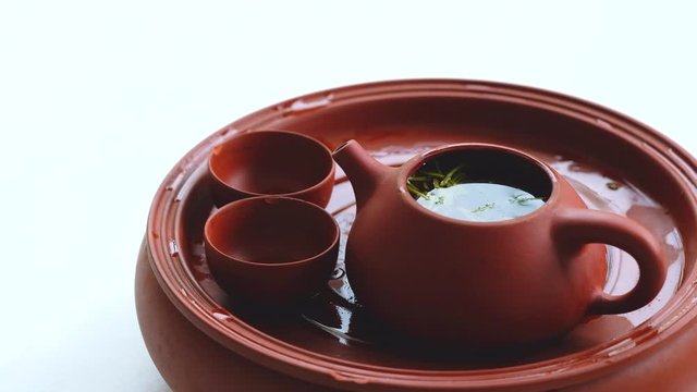 Close up red brown ceramic clay fired teapot and teacups on white background. Fresh longjing tea leaves floating on peaceful tea water. Traditional Chinese tea culture concept