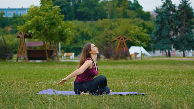 Young caucasian woman relaxing by practicing yoga at outdoor place in the morning. Beautiful woman doing yoga in the park at green grass