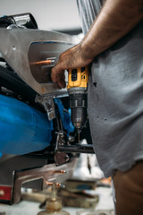 Male worker drill a hole in motorcycle metal part at the workshopauto, automobile, car, check, engine, garage, hand, inspection, job, maintenance, man, mechanic, motor, people, person, repair, service