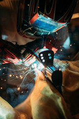 Industrial Worker with protective gloves and Welded Iron Mask welding motorcycle metal steel part at the factory workshop
