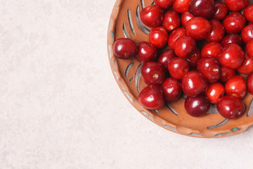 Red sweet cherry in a clay plate on a cream table