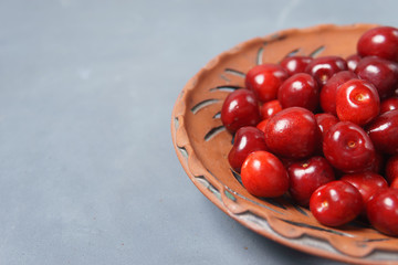 Red sweet cherry in a clay plate on a gray table