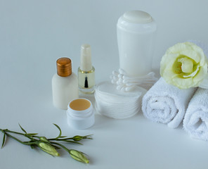 Fototapeta na wymiar Close up of the set for body care: a few rolled towels, antiperspirant, cotton pads, cotton buds, bottle of lotion, balsam for lips, nail polish with eustoma on the white background