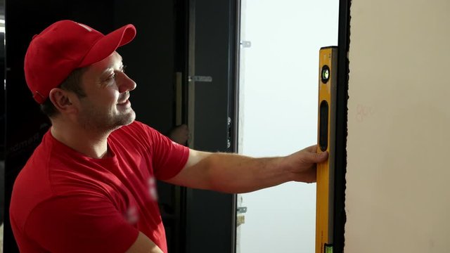 a man, a Builder, in a red cap and t-shirt, uses a Ruler level clinometer bubbles, carefully looking to measure the evenness of the wall, in the doorway. slow shooting