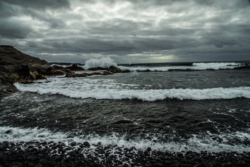  beautyful view from a stony shore to a raging ocean wave during a spring storm with a horizon line and little sunray in the grey sky in afternoon