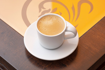 Closeup to white cup of espresso coffee on glass and wooden table 