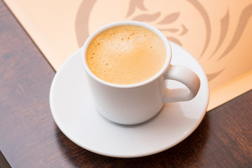 Closeup to white cup of espresso coffee on glass and wooden table 
