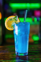 Blue cocktail in a high glass glass with a slice of orange. Colourful cocktail on the dark back. Cocktail on a Colourful  background in a tall glass.