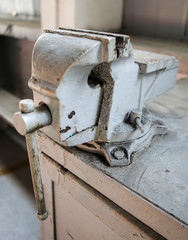Shallow depth of field image with a rusty and dirty heavy iron vice on a workbench inside a workshop with no people around