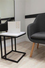 Grey armchair and minimalistic table white and black with metal construction.Book on table with sample of text.Concept