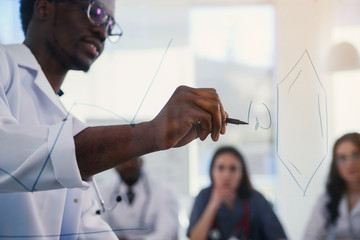 African professor at medical conference in modern clinic teaches his students. Doctor writing on...