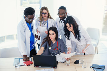 Multinational group of doctors looks at something in the laptop. A female doctor is sitting at the...