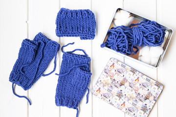 Knitted mittens withiout fingers. Woolen yarn ball. White wooden background. Copy space. Place for text. Top view.  Metal box with cotton