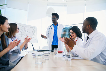 International group of professional young doctors are clapping their hands and smiling at a medical conference in a modern clinic. Medicine and healthcare concept.