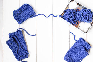 Knitted mittens withiout fingers. Woolen yarn ball. White wooden background. Copy space. Place for text. Top view.  Metal box with cotton