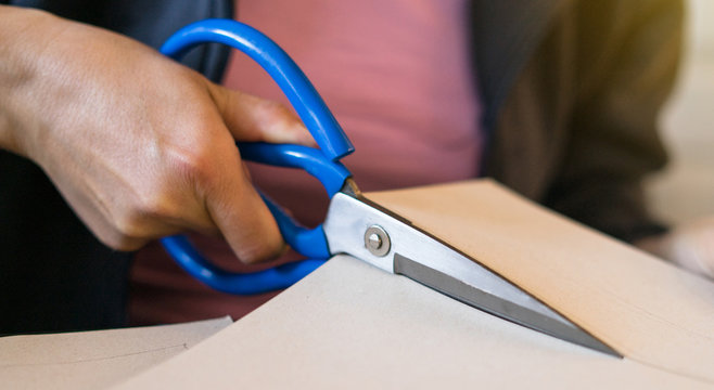 Close up on hands holding paper cardboard cutting using scissors at home office