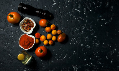 Vegetables on a dark background. Spices, oil, zucchini, tomato, peaches on a dark textured surface. View from above. copy space.