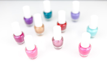 Table top view on a white desk full of small assorted glass and plastic bottles with nail polish and lacquer.