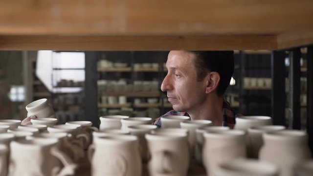 Caucasian male potter coming to the shelves and taking handmade cap.