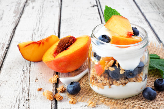 Healthy peach and blueberry parfait in a mason jar, close up on a white wood background