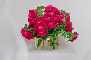 Lavish bouquet of wild tea roses in ball glass vase standing on the background of white cloth.