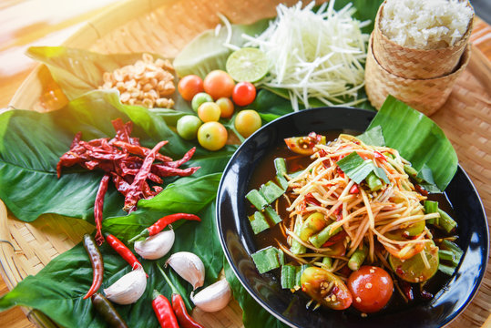Papaya salad served on wooden dining table / Green papaya salad spicy thai food on plate with sticky rice herbs and spices ingredients with chilli tomato peanut garlic Som tum Thai menu Asian food