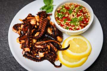 Octopus salad with lemon herbs and spices on white plate - Tentacles squid grilled appetizer food hot and spicy chilli sauce seafood cooked served on dark background , top view
