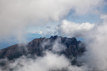 Aerial view of Mt Arrowsmith surrounded by clouds during a vibrant sunny summer day. Taken near Nanaimo and Port Alberni, Vancouver Island, British Columbia, Canada.