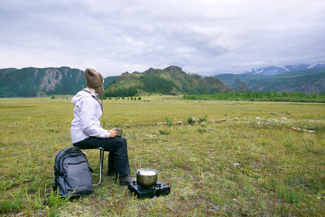 Naklejka na ściany i meble Woman traveler drinks coffee or tea with a view of the mountain landscape. The concept of active recreation and tourism in the mountains.