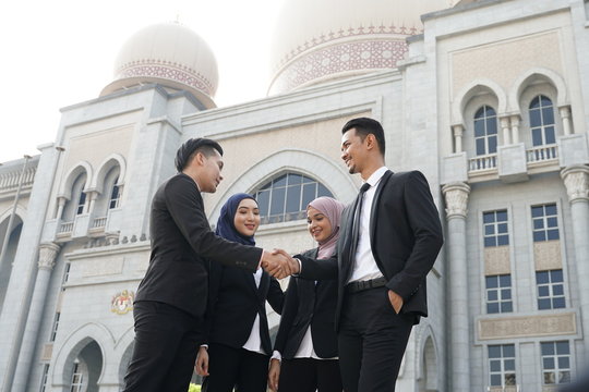Muslim Asian business people shaking hands with new partner, business co-working teamwork concept. Successfull entrepreneur over a blur majestic building