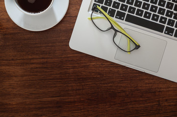 Top view wooden table with labtop, eyegalsses and a cup of black coffee.