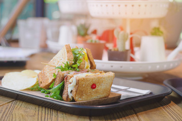 Club sandwich with bacon - chicken, fie egg, cheese, potato and lettuce on wooden tabel in cafe background.