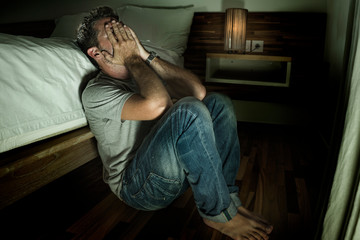 Fototapeta premium dramatic home portrait of young desperate and depressed lonely man sitting on bedroom floor crying sick suffering anxiety crisis and depression problem feeling helpless