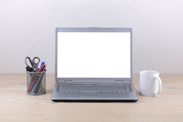 Fototapeta premium Laptop computer on office desk coffee mug and pens. White screen template with clipping path