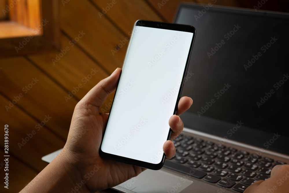 Poster mockup mobile phone image. close up hands using modern smart phone technology with blurred laptop ba