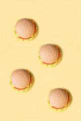 Plastic burger, salad, tomato, on a yellow background. Vertical orientation. Children's toy. The concept of harmful artificial food. Plastic Not organic. Not healthy.