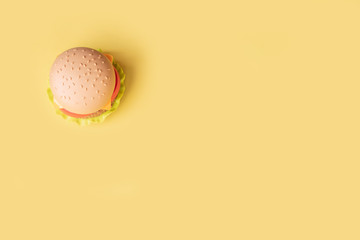 Plastic burger, salad, tomato, on a yellow background. Vertical orientation. Children's toy. The concept of harmful artificial food. Plastic Not organic. Not healthy. Copy space