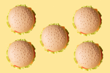 Plastic burger, salad, tomato, on a yellow background. Vertical orientation. Children's toy. The concept of harmful artificial food. Plastic Not organic. Not healthy.