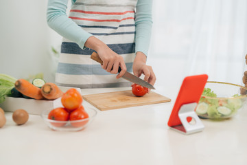 The young happy woman in apron looking at recipe in tablet in the kitchen. Vegetable salad. Dieting concept. Healthy lifestyle. Cooking at home. Prepare food.