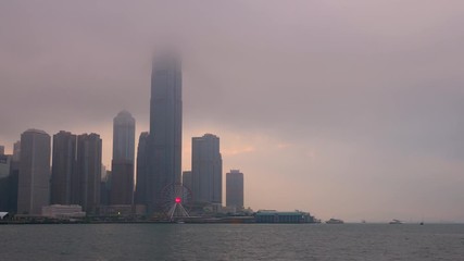 Time lapse of Hong Kong cityscape with sun light in the hard mist at the harbor in the raining day