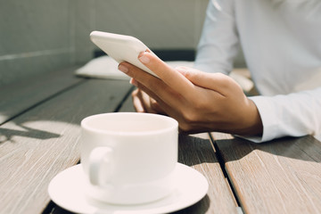 Female hand using mobile phone over wooden table at coffee shop