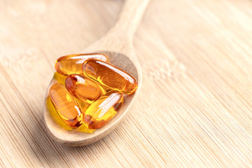 Fish oil capsules as a dietary supplement containing omega-3 and vitamin a is high for health care. Salmon oil into spoon on the wood table.