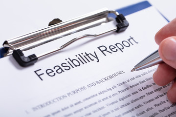 Person's Finger Holding Pen Over Feasibility Report