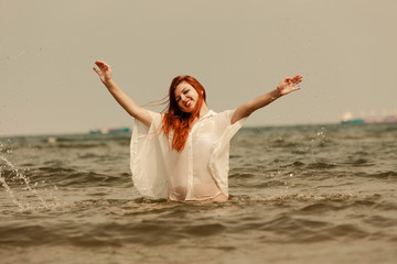 Fototapeta na wymiar Redhead woman playing in water during summertime