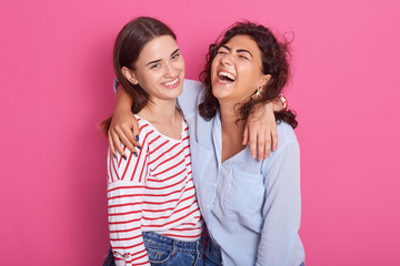 Close up portrait of happy lesbian girls hugging each other, have satisfied expessions, being in high spirit, wearing casual shirts isolated on pink background. Same sex love and relationship concept.