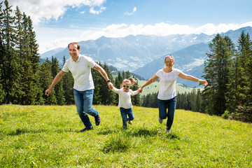 Family With Daughter Running On Field In Mountains