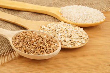 Buckwheat, rice and rolled oats in wooden spoon on jute and wooden background