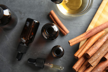 Composition with cinnamon essential oil on grey table, flat lay