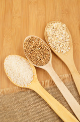 Buckwheat, rice and rolled oats in wooden spoon on jute and wooden background