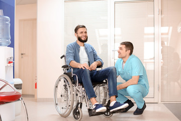 Male doctor taking care of man in wheelchair indoors